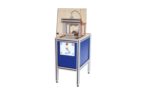 The Shear and Compression Test Apparatus is a compact industrial machine with a blue panel, control buttons, and a transparent safety cover over the testing area, supported by four metal legs against a plain white background.