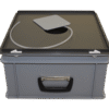 The Tube Dispenser is a grey plastic box with a black lid featuring a circular cut-out, a flexible tube, a rectangular grey pad, and a black front handle.