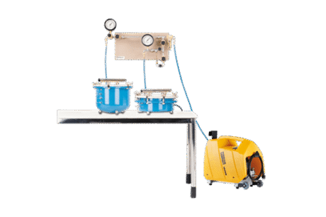 A Ceramic Plates Set for PF Determination (PF 2.0-4.2), featuring gauges and blue chambers on a table, is connected by blue hoses to a yellow vacuum pump positioned on the floor beside the table.