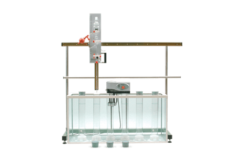 A Pipette Apparatus is set up in a laboratory with a water tank, vertical rods, and multiple containers in front of the tank, all against a plain white background.